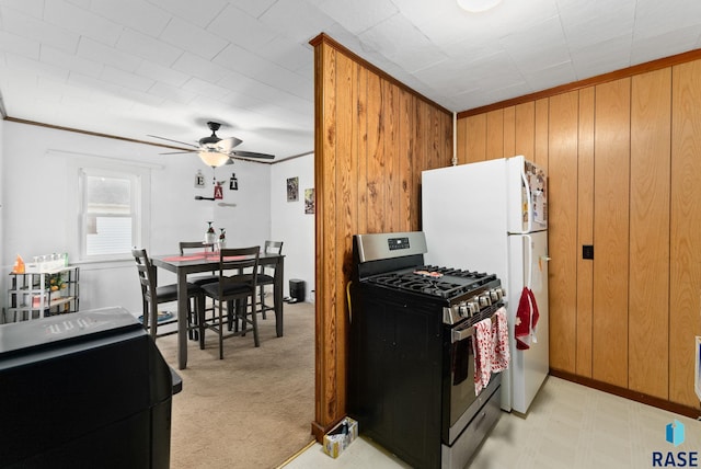 kitchen with crown molding, ceiling fan, stainless steel range with gas cooktop, light colored carpet, and wood walls