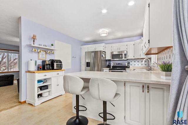 kitchen with sink, appliances with stainless steel finishes, a kitchen breakfast bar, tasteful backsplash, and white cabinets