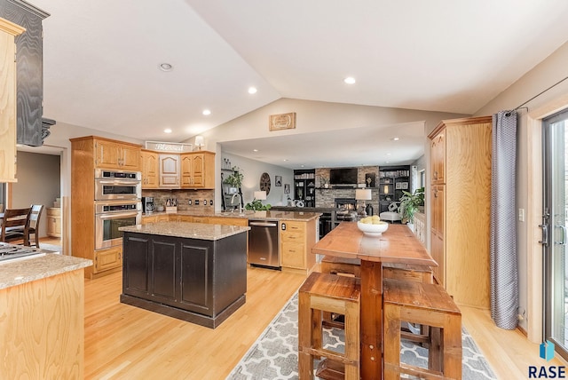 kitchen with vaulted ceiling, appliances with stainless steel finishes, a center island, kitchen peninsula, and light wood-type flooring