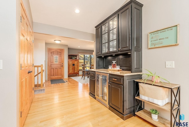 kitchen featuring light stone countertops, light wood-type flooring, beverage cooler, and dark brown cabinetry