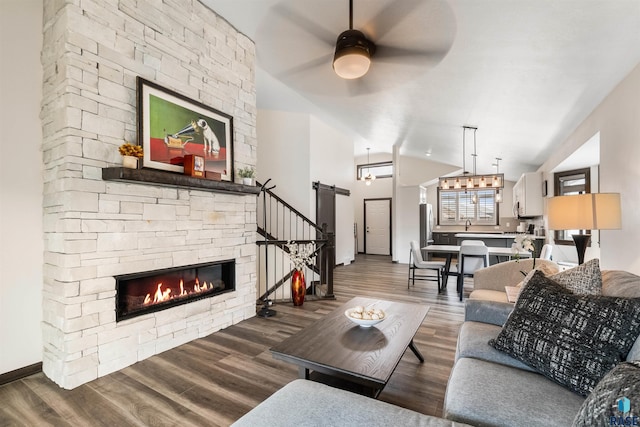 living room featuring a stone fireplace, lofted ceiling, dark hardwood / wood-style flooring, ceiling fan, and a barn door