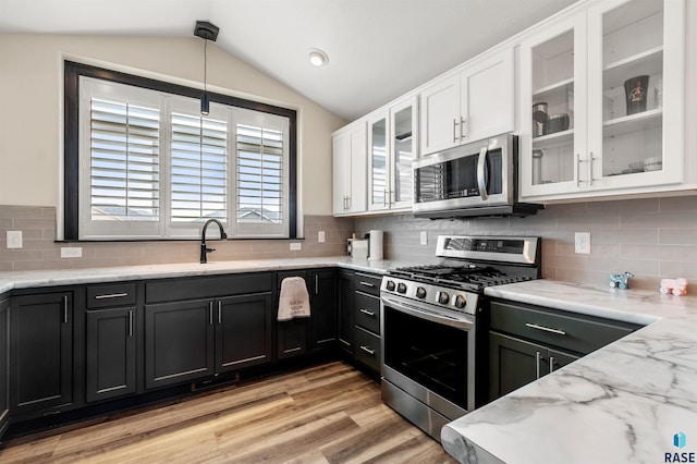 kitchen with decorative light fixtures, vaulted ceiling, light hardwood / wood-style flooring, appliances with stainless steel finishes, and white cabinets