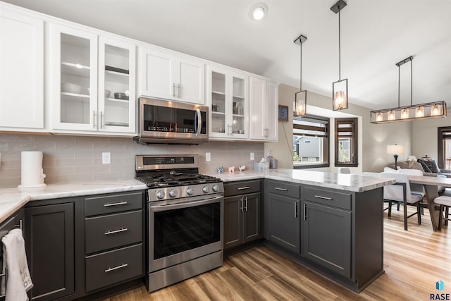 kitchen with hardwood / wood-style floors, white cabinetry, backsplash, hanging light fixtures, and stainless steel appliances