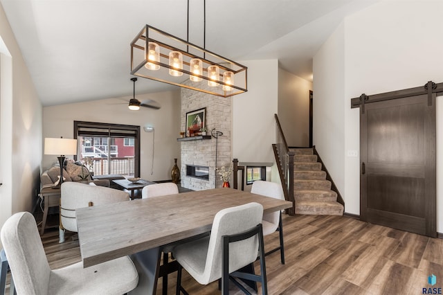 dining area with hardwood / wood-style flooring, ceiling fan, a fireplace, vaulted ceiling, and a barn door