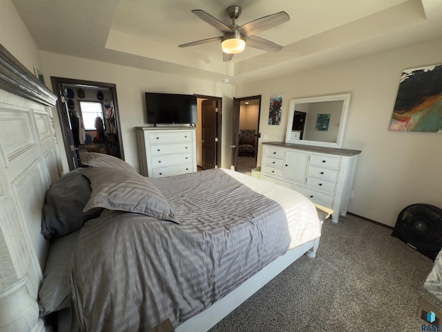 carpeted bedroom with a tray ceiling, a closet, ceiling fan, and a spacious closet