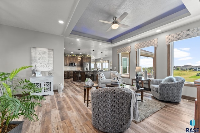 living room with light hardwood / wood-style flooring, plenty of natural light, and a raised ceiling