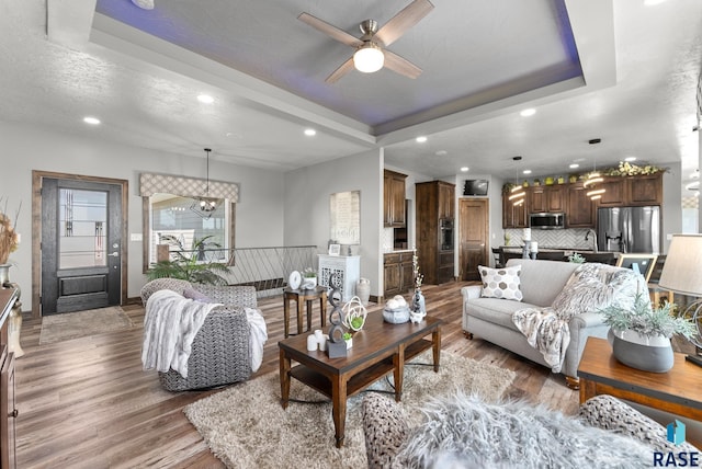 living room with hardwood / wood-style flooring, ceiling fan with notable chandelier, a raised ceiling, and a textured ceiling