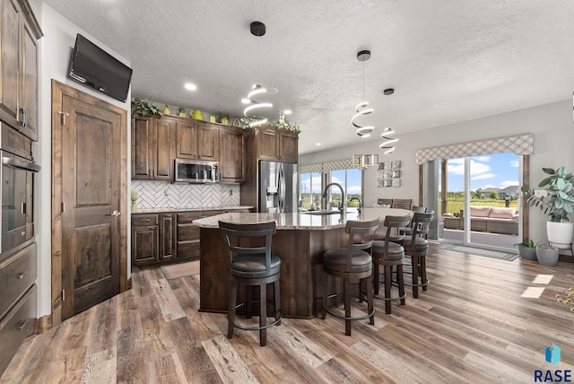 kitchen with appliances with stainless steel finishes, decorative light fixtures, a kitchen breakfast bar, decorative backsplash, and a kitchen island with sink