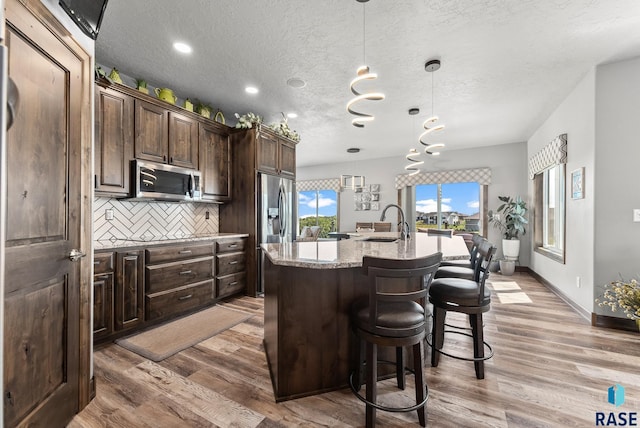 kitchen with decorative light fixtures, appliances with stainless steel finishes, a kitchen breakfast bar, an island with sink, and decorative backsplash