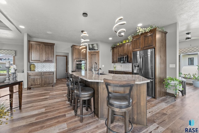 kitchen with sink, hanging light fixtures, appliances with stainless steel finishes, an island with sink, and decorative backsplash