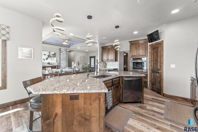 kitchen featuring an island with sink, sink, a tray ceiling, stainless steel appliances, and light wood-type flooring