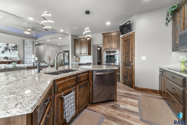 kitchen with sink, light hardwood / wood-style flooring, appliances with stainless steel finishes, a kitchen island with sink, and hanging light fixtures