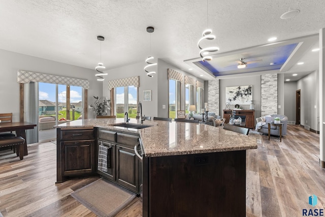 kitchen featuring pendant lighting, sink, a kitchen island with sink, a tray ceiling, and light stone countertops