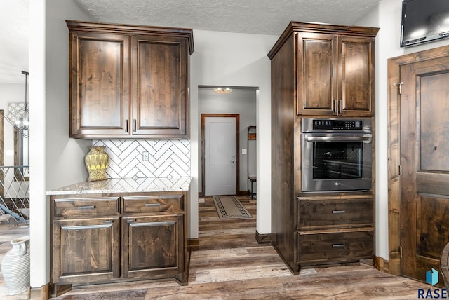 kitchen featuring dark wood-type flooring, tasteful backsplash, dark brown cabinets, a textured ceiling, and oven