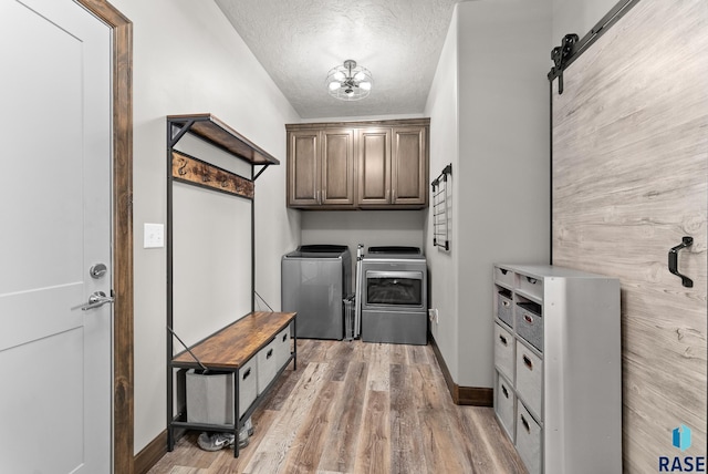 laundry room with hardwood / wood-style floors, washing machine and dryer, cabinets, a textured ceiling, and a barn door