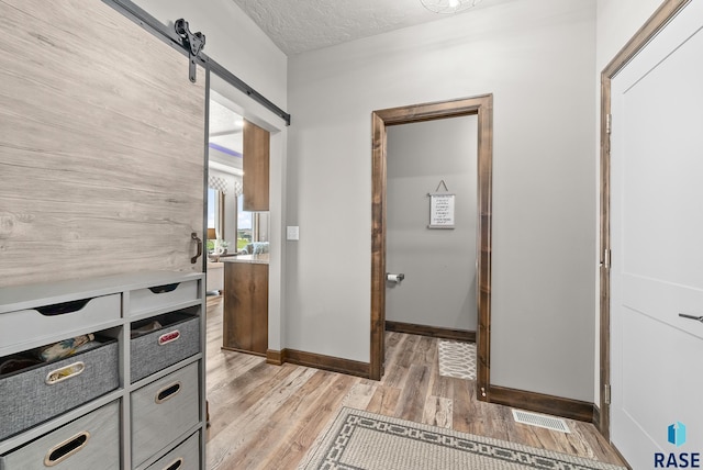 corridor featuring a barn door, a textured ceiling, and light wood-type flooring