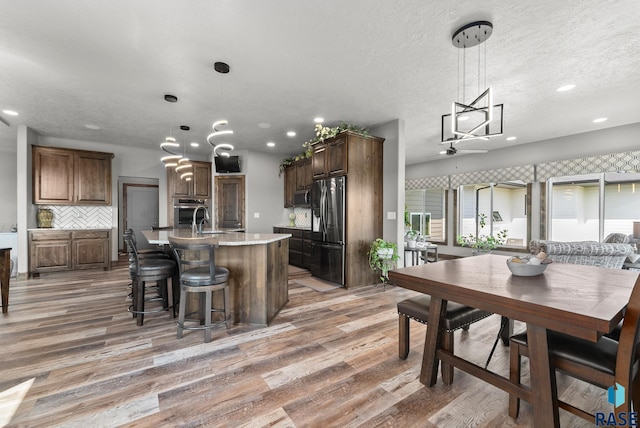 kitchen with hardwood / wood-style floors, appliances with stainless steel finishes, an island with sink, and hanging light fixtures