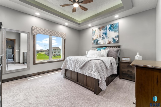 bedroom with light colored carpet, a textured ceiling, ceiling fan, and a tray ceiling