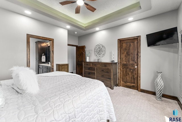 bedroom with a tray ceiling, ensuite bath, ceiling fan, and carpet