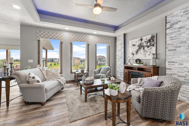 living room with ceiling fan, a tray ceiling, hardwood / wood-style floors, and a textured ceiling