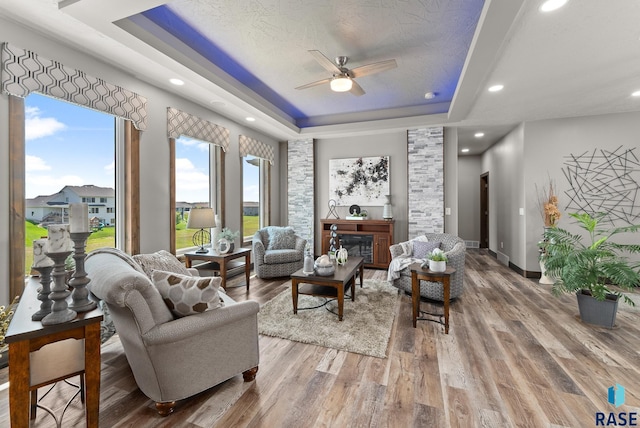 living room featuring ceiling fan, a tray ceiling, hardwood / wood-style floors, and a textured ceiling