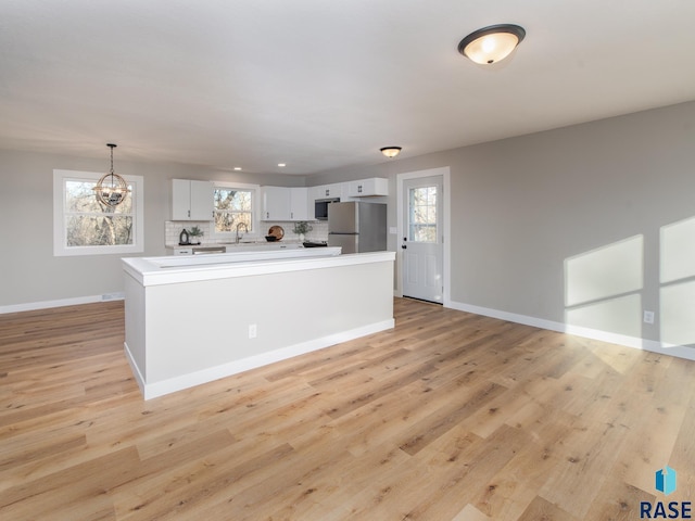 kitchen with tasteful backsplash, white cabinetry, stainless steel fridge, hanging light fixtures, and a notable chandelier