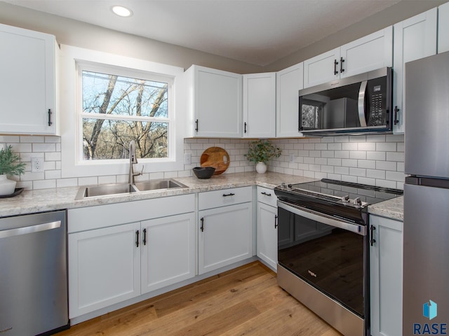 kitchen featuring sink, light hardwood / wood-style flooring, stainless steel appliances, tasteful backsplash, and white cabinets