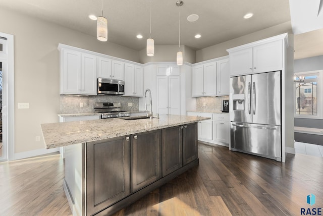 kitchen featuring appliances with stainless steel finishes, an island with sink, sink, white cabinets, and light stone counters