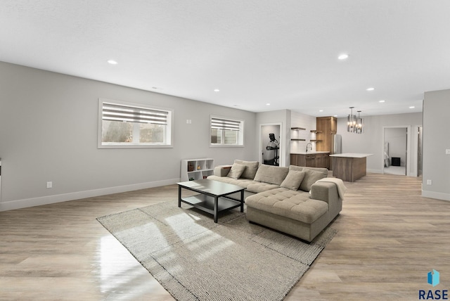 living room featuring an inviting chandelier, sink, and light hardwood / wood-style flooring