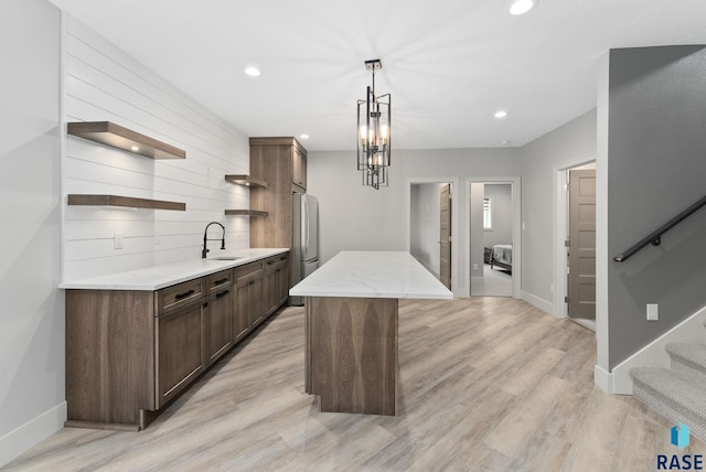 kitchen featuring a kitchen island, pendant lighting, stainless steel refrigerator, dark brown cabinets, and light wood-type flooring