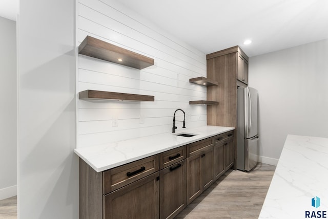 kitchen featuring sink, stainless steel fridge, dark brown cabinets, light stone counters, and light hardwood / wood-style floors