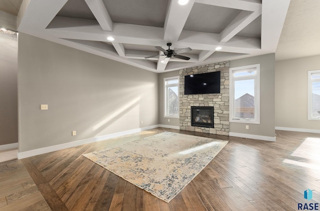 living room with dark wood-type flooring, coffered ceiling, a stone fireplace, ceiling fan, and beam ceiling