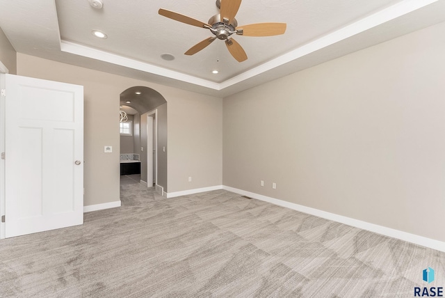 spare room with ceiling fan, a tray ceiling, and light carpet