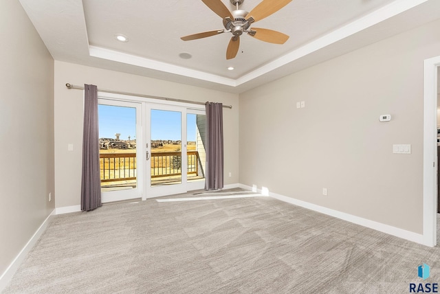 empty room with light carpet, a tray ceiling, and ceiling fan