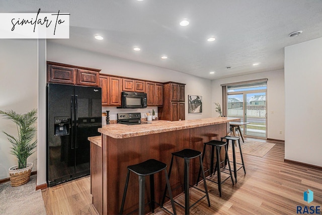 kitchen with light hardwood / wood-style flooring, a breakfast bar, a center island with sink, and black appliances