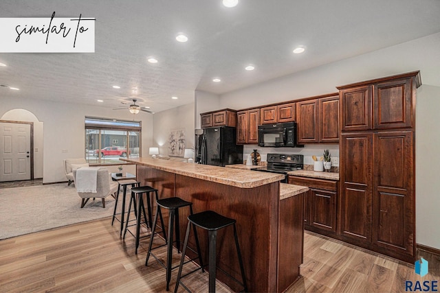 kitchen featuring light hardwood / wood-style flooring, a breakfast bar, ceiling fan, black appliances, and a center island with sink