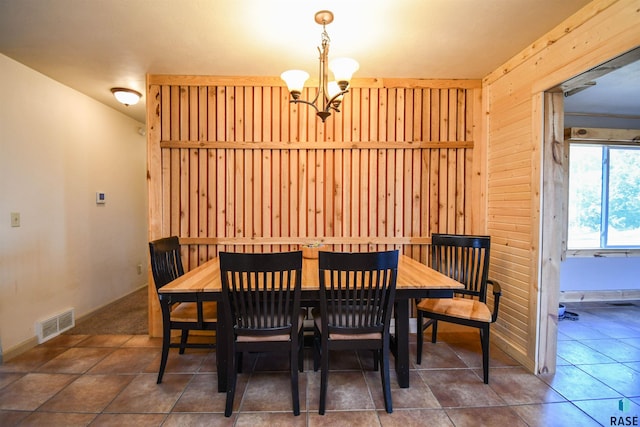 dining area featuring a notable chandelier, dark tile patterned floors, and wood walls