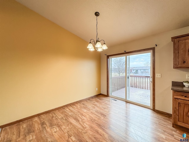 unfurnished dining area with lofted ceiling, an inviting chandelier, and light hardwood / wood-style flooring