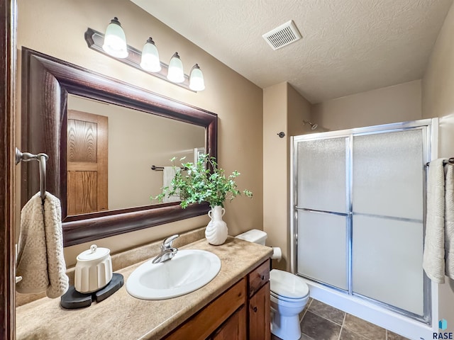 bathroom with toilet, a textured ceiling, vanity, a shower with door, and tile patterned flooring