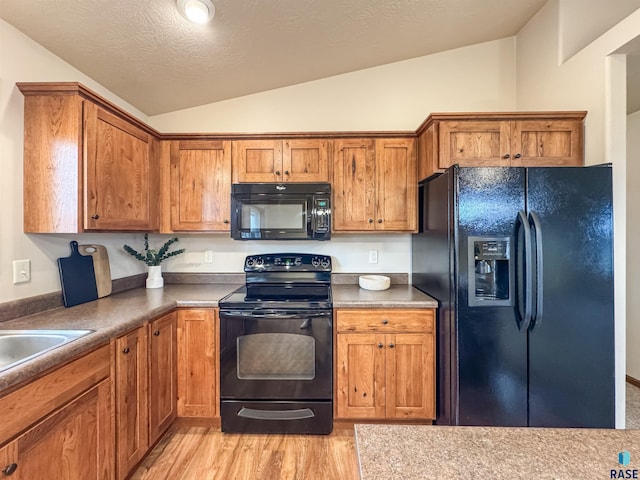 kitchen with sink, vaulted ceiling, a textured ceiling, light hardwood / wood-style floors, and black appliances