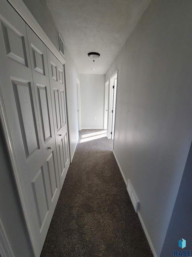 hallway with dark carpet and a textured ceiling