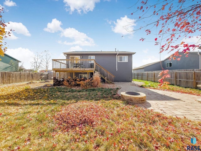 back of property with a wooden deck, a lawn, a patio area, and an outdoor fire pit