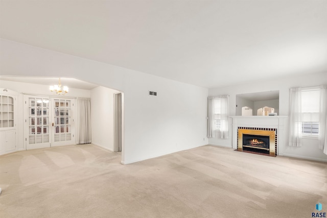 unfurnished living room featuring an inviting chandelier, light colored carpet, and a fireplace