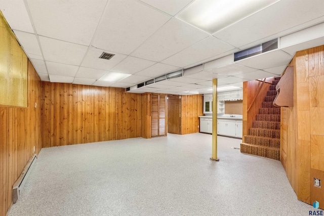 basement featuring a drop ceiling, a baseboard heating unit, and wooden walls