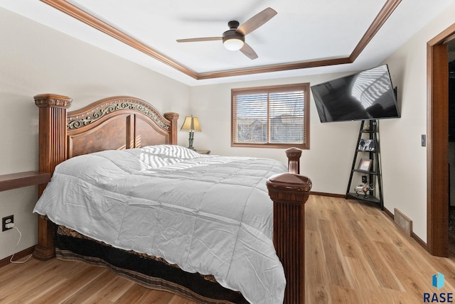 bedroom with light hardwood / wood-style floors, a raised ceiling, and ceiling fan