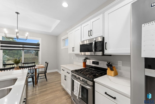 kitchen with pendant lighting, appliances with stainless steel finishes, light stone counters, white cabinets, and light wood-type flooring