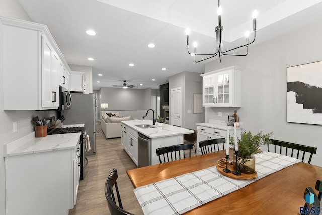 dining room with ceiling fan with notable chandelier, sink, and light wood-type flooring