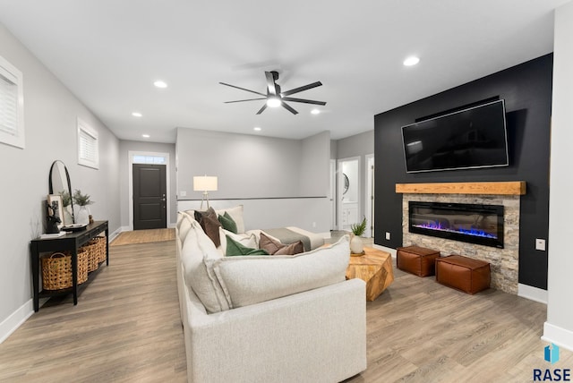 living room featuring ceiling fan, a stone fireplace, and light wood-type flooring