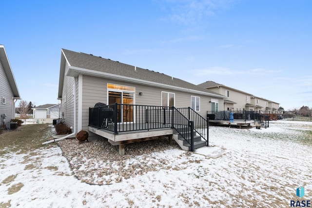 snow covered house with a wooden deck, cooling unit, and a trampoline