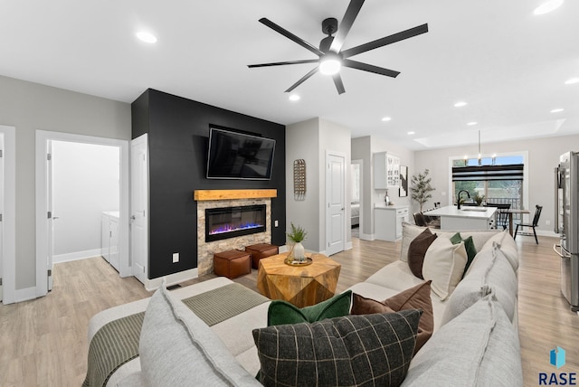 living room featuring sink, a stone fireplace, ceiling fan, and light wood-type flooring